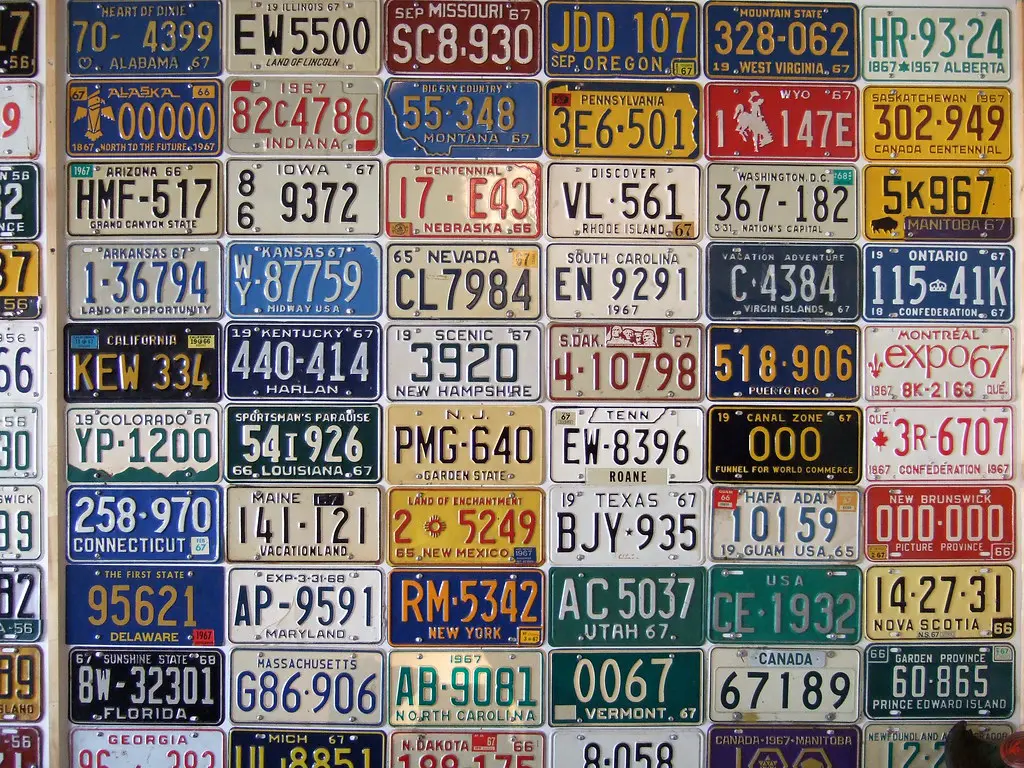 Rows of 1967 license plates from U.S. states and Canadian provinces on a garage wall